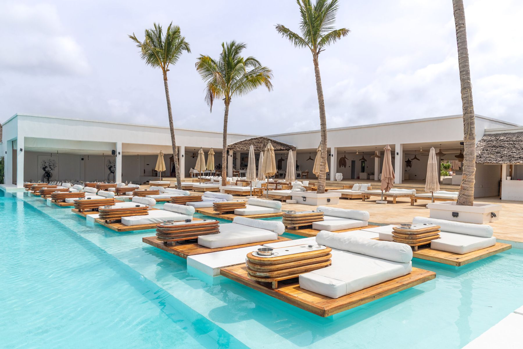 Floating wooden sunbeds in the turquoise pool at Le Saint Tropez Beach Club, framed by palm trees