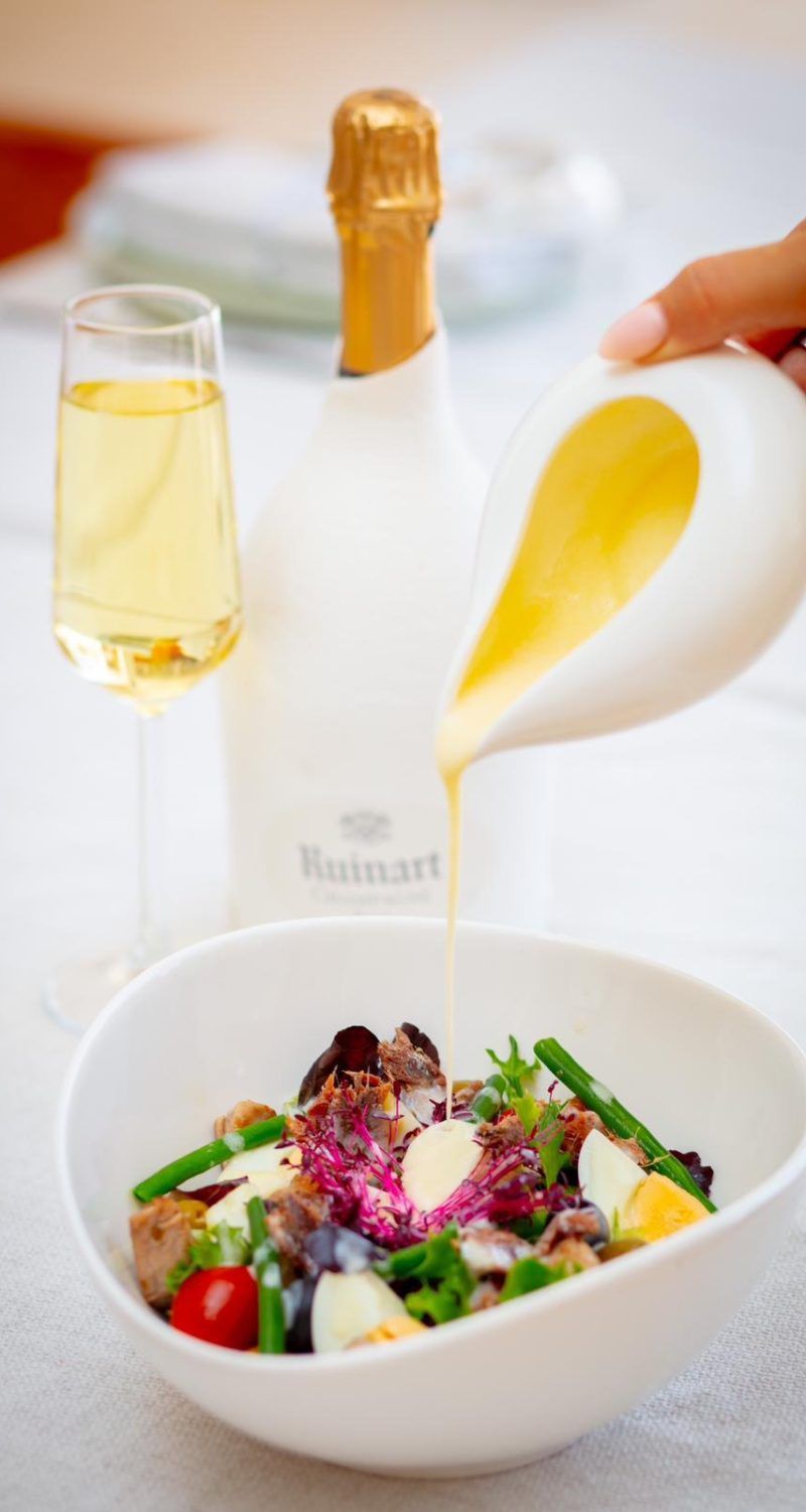 A fresh salad being dressed beside a bottle of champagne
