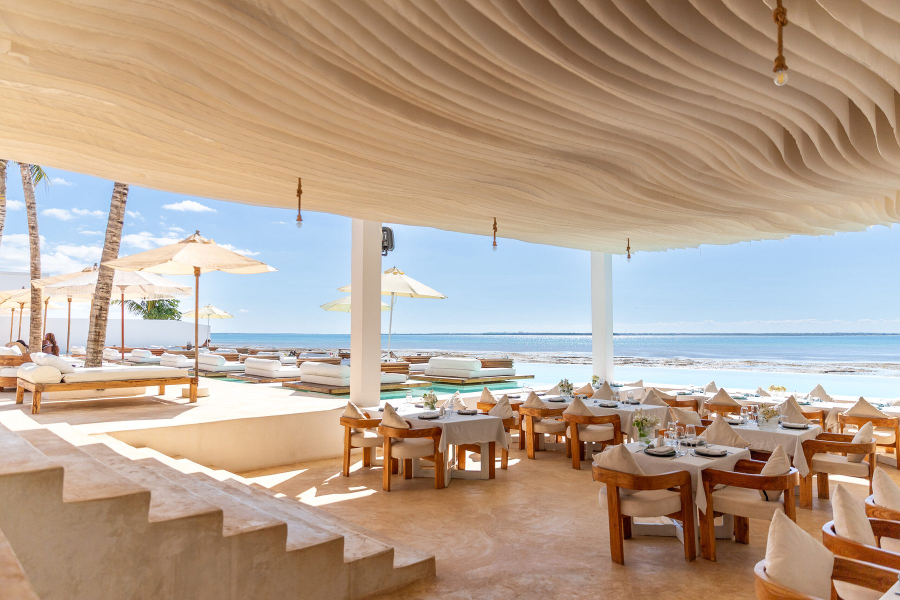 The oceanfront restaurant terrace beneath a sculpted rippled ceiling, opening onto the Indian Ocean